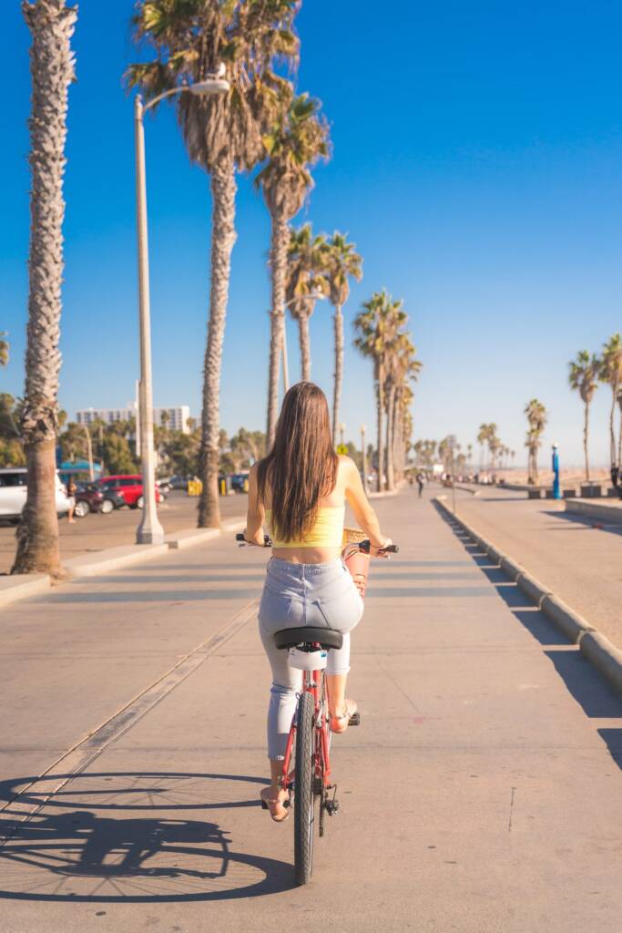 Una joven se aleja en bicicleta por un largo paseo bordeado de palmeras, junto al mar
