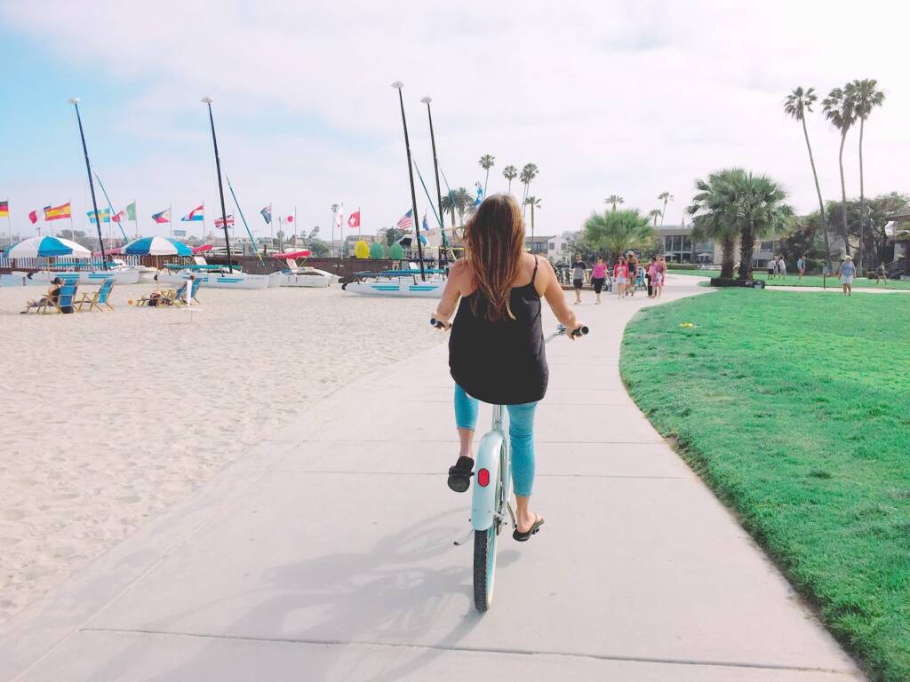 Una ciclista circula por un paseo adoquinado junto a la playa, entre veleros y palmeras, cerca de Torrevieja
